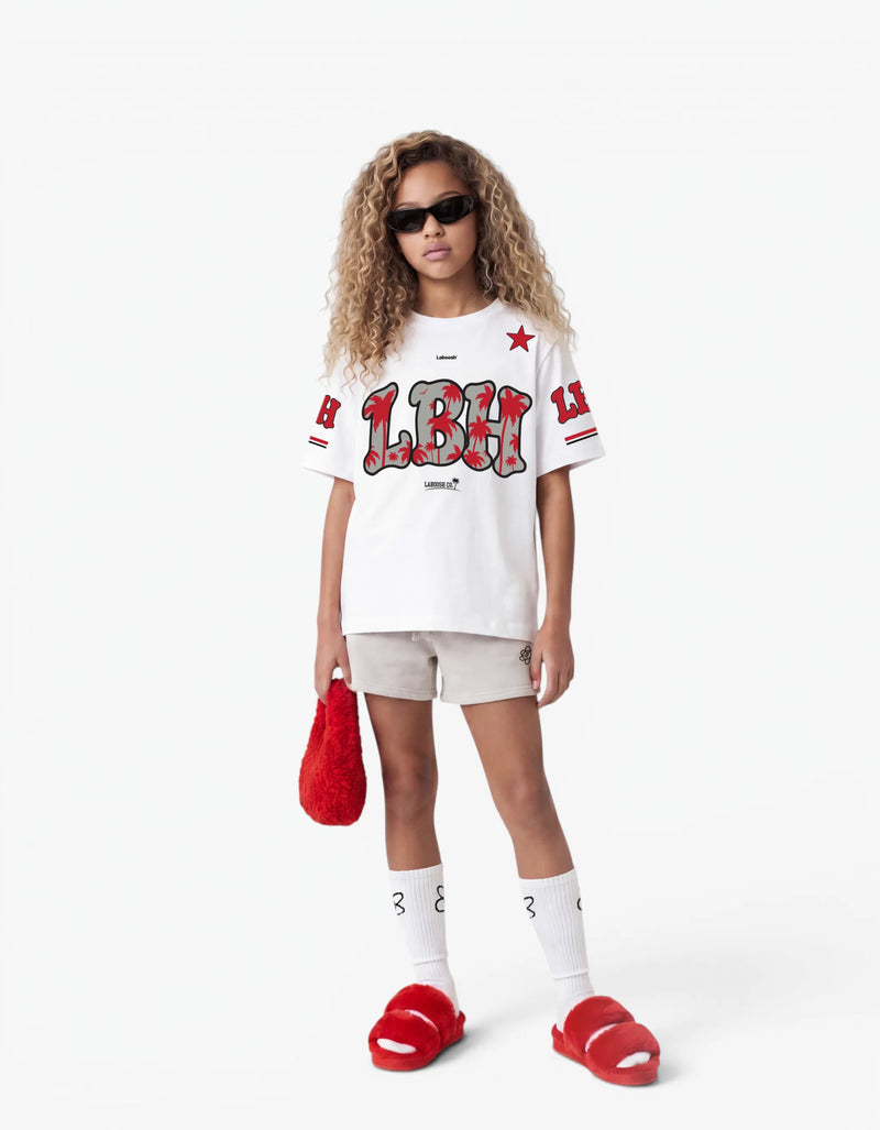 Girl wearing the white LBH oversized t-shirt with red palm-tree graphic and Laboosh™ logo on the chest, front view, styled with matching grey shorts on a white background. — alt view