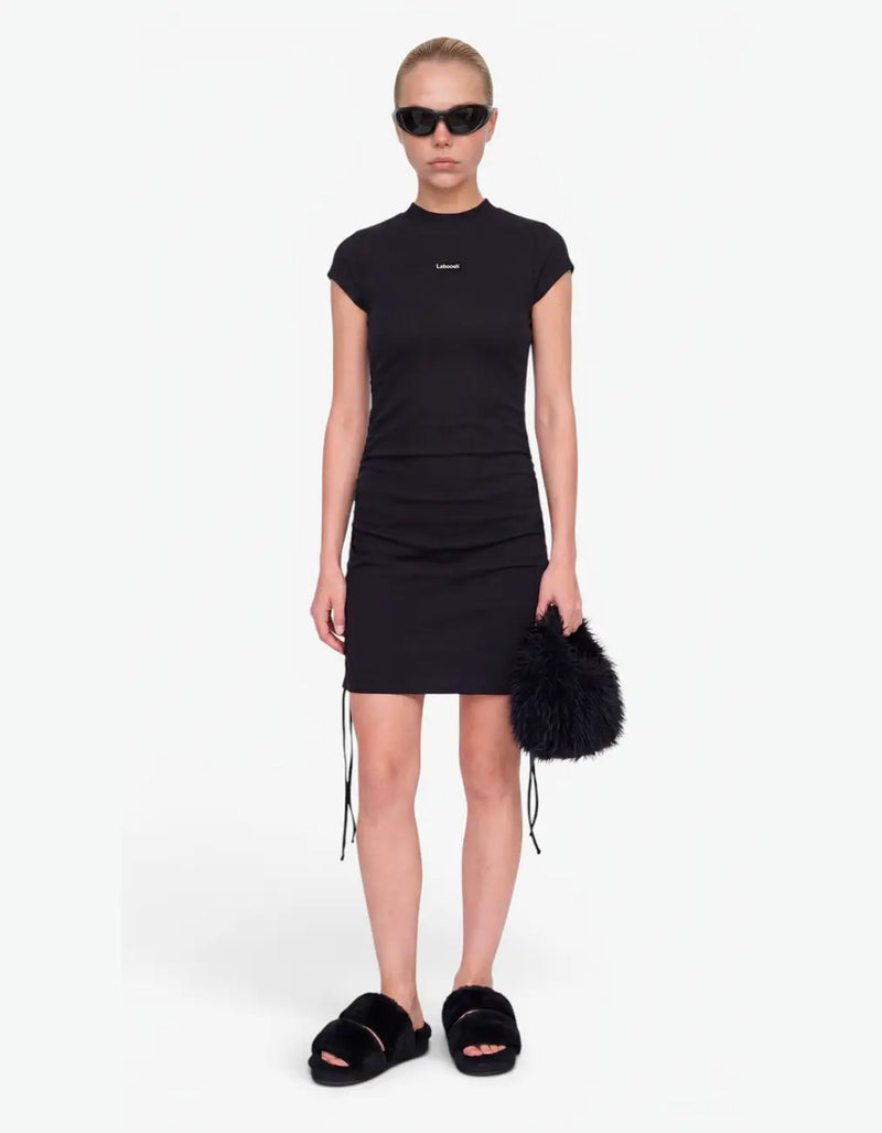 Girl wearing a black ribbed ruched dress with short sleeves and Laboosh™ logo on the chest, front view on a white background