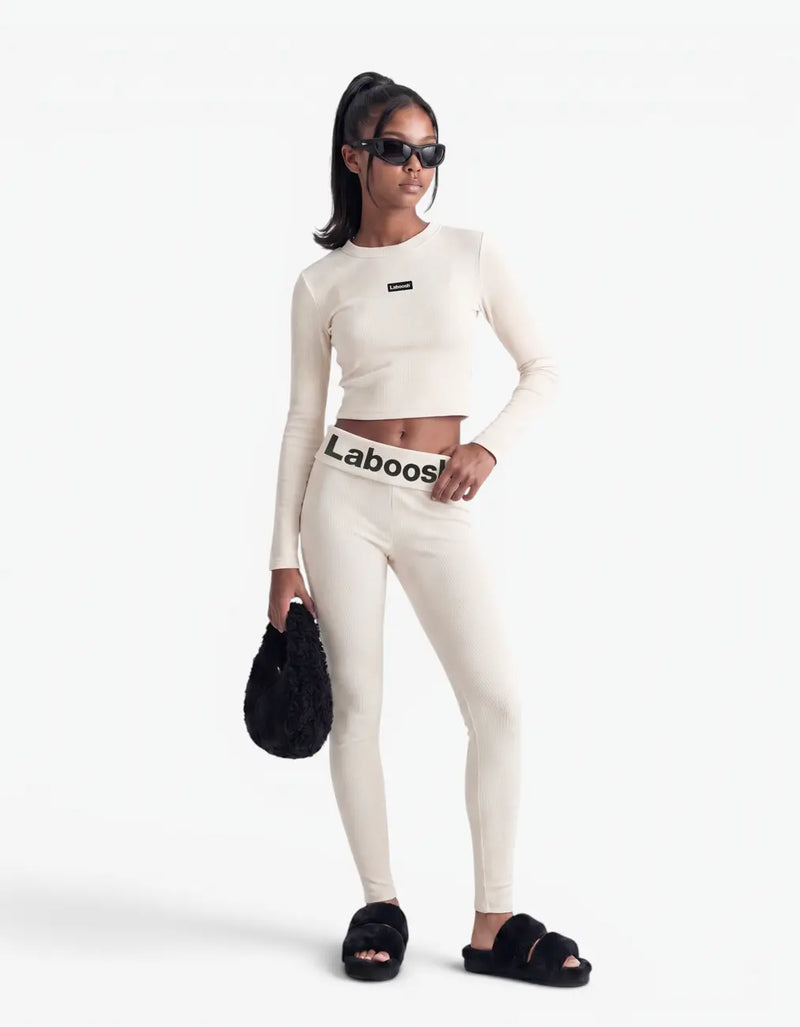 Girl wearing cream ribbed long leggings and matching long-sleeve crop top with Laboosh™ branding on the waistband, front view on a white background