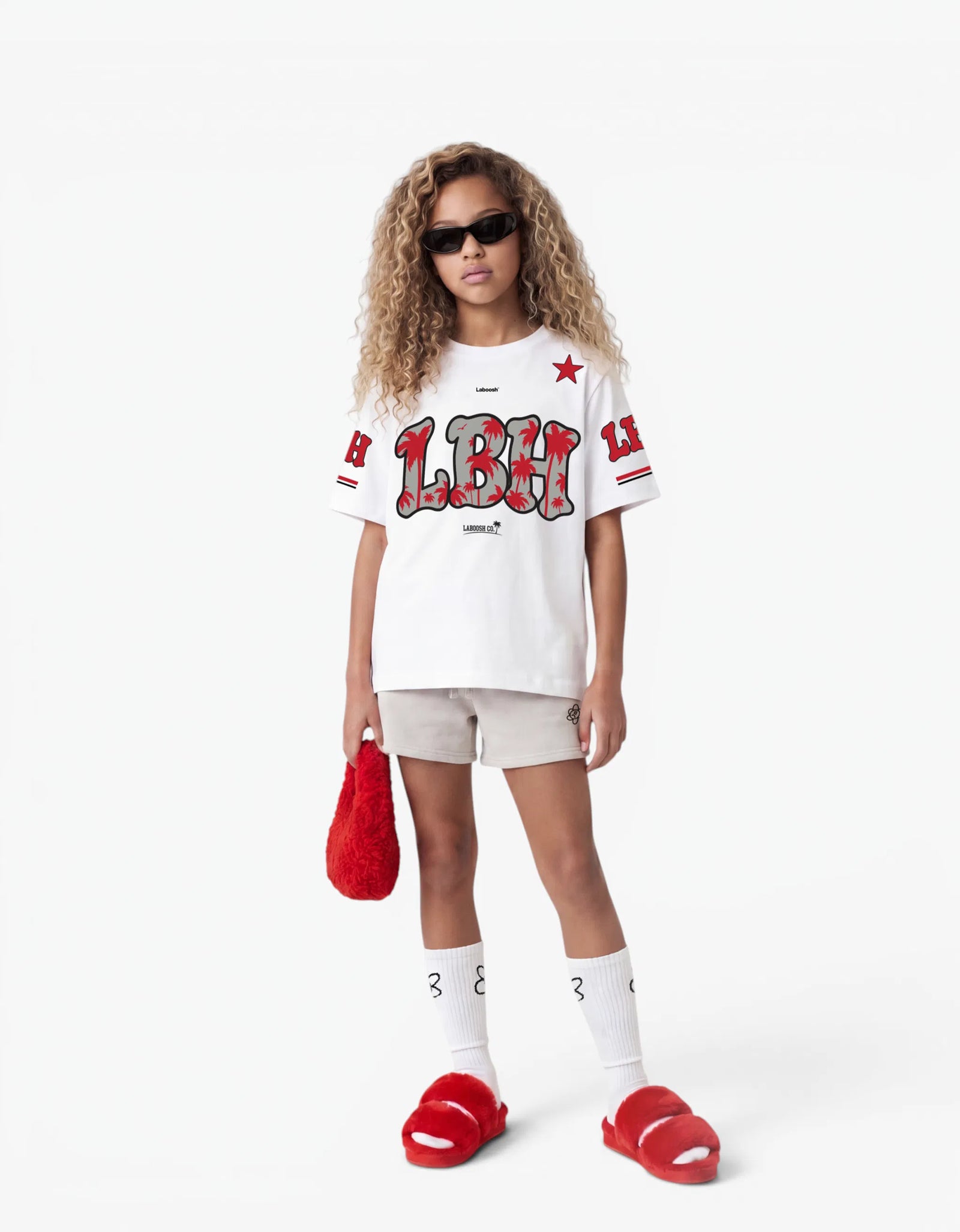 Girl wearing the white LBH oversized t-shirt with red palm-tree graphic and Laboosh™ logo on the chest, front view, styled with matching grey shorts on a white background.