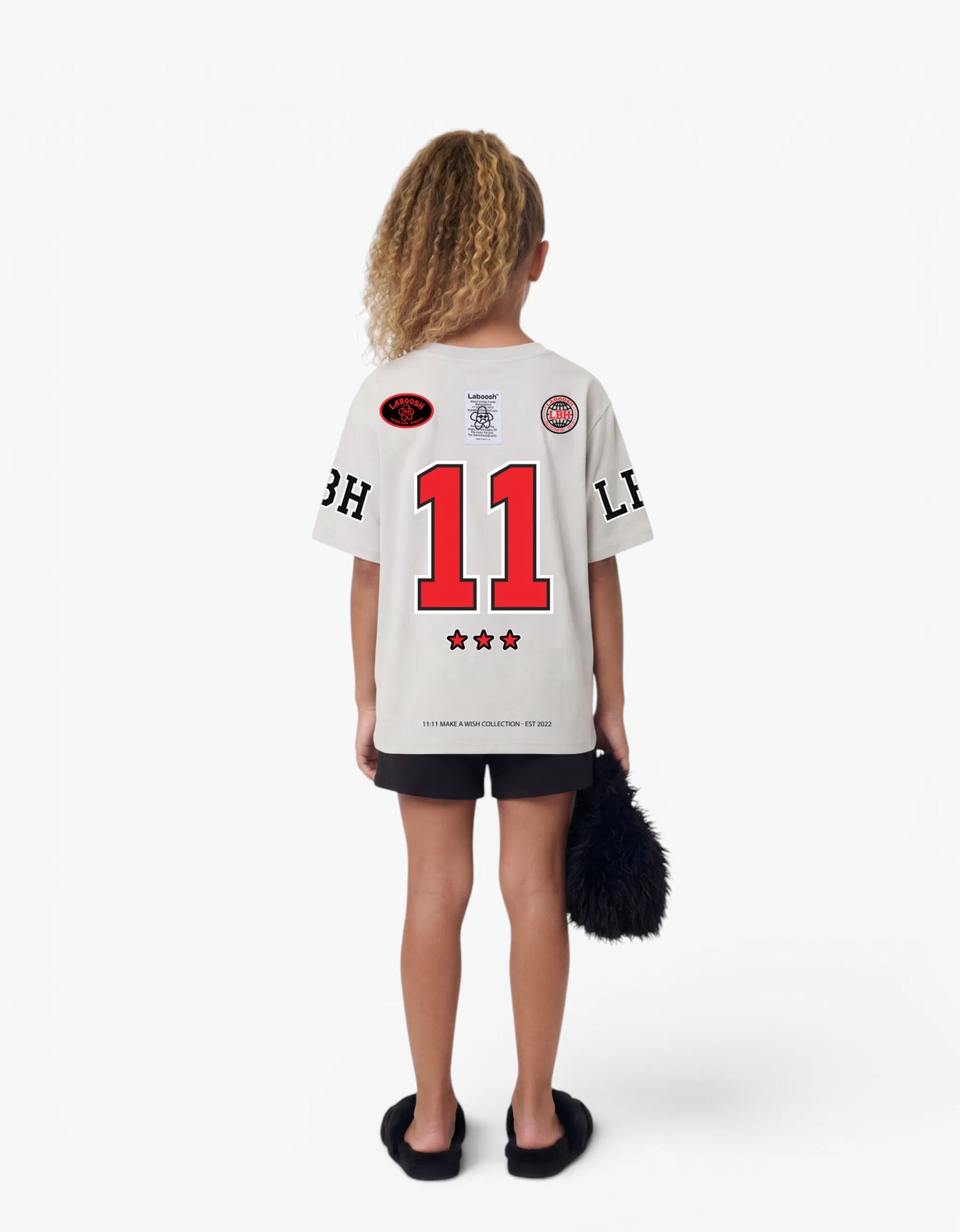 Girl in cream t-shirt from Rib Collection, back view, with a signature Laboosh™ print, against a bright white background.