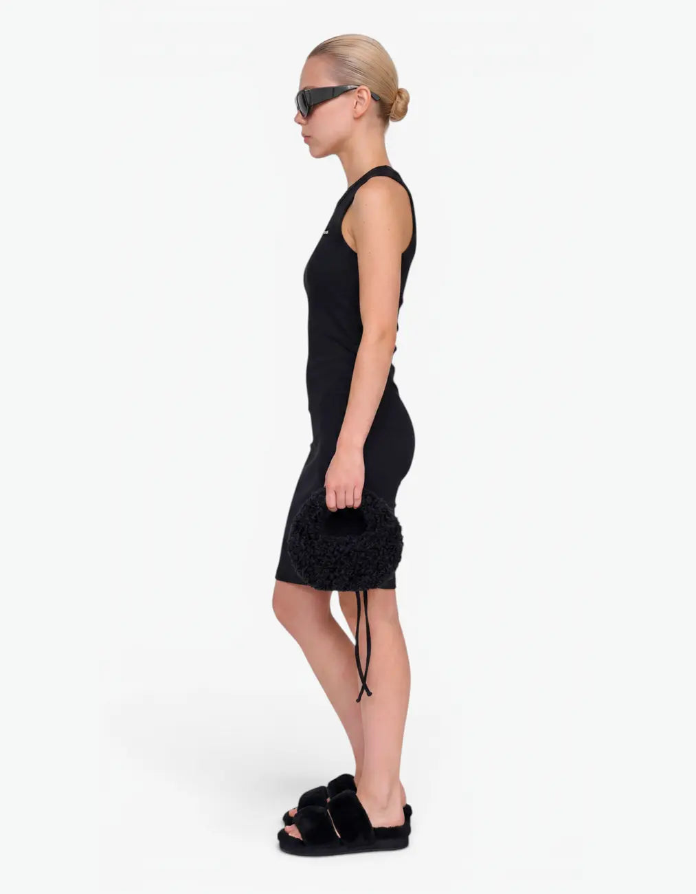 Side view of a girl wearing the black ribbed ruched dress, showing the sleeveless silhouette and ruched seam, on a white background