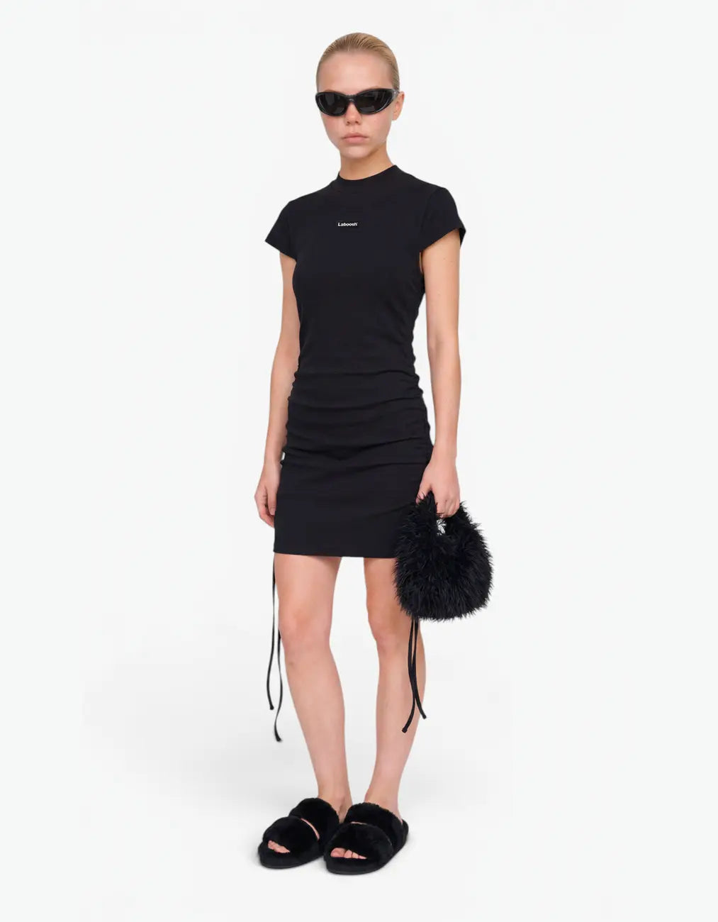 Girl wearing a black ribbed ruched dress with short sleeves and Laboosh™ branding, styled with a faux-fur bag, front view on a white background