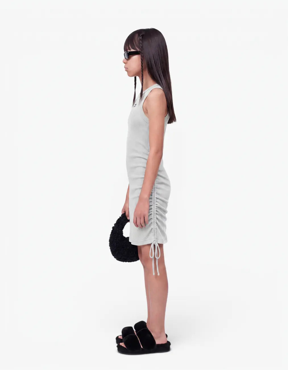 Side view of a girl wearing the grey ribbed ruched dress, showing the sleeveless silhouette and ruched side seam, on a white background