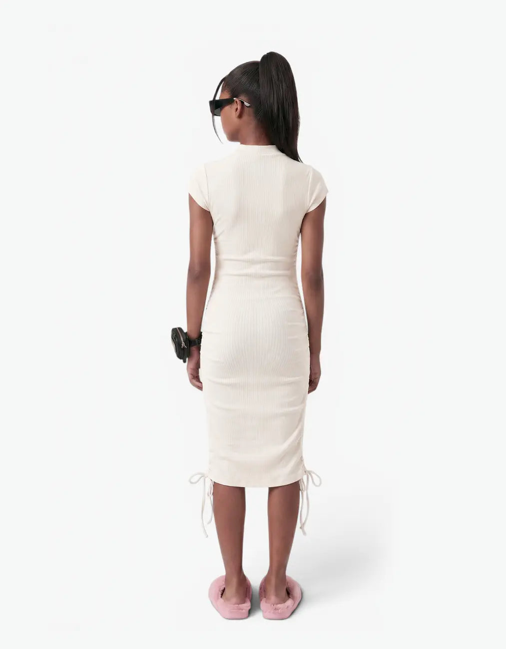 Back view of a girl wearing the cream ribbed ruched dress showing the fitted ribbed back and ruched hem ties, on a white background